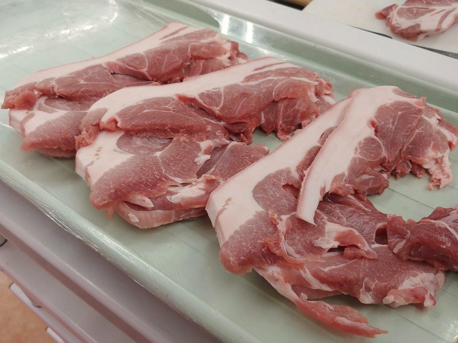Raw pork shoulder steaks laid on a pale tray