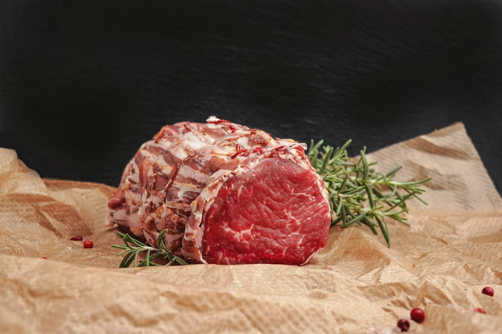 A beef roast tied with string resting on brown wrapping paper with rosemary