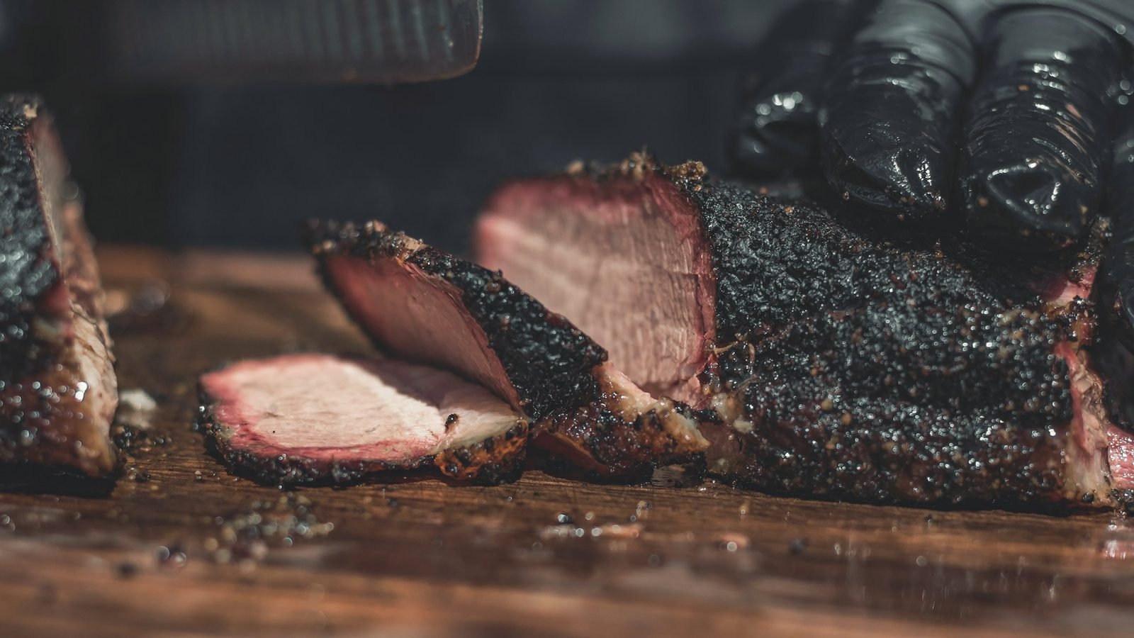 A smoked brisket with a dark bark being sliced on a wooden board