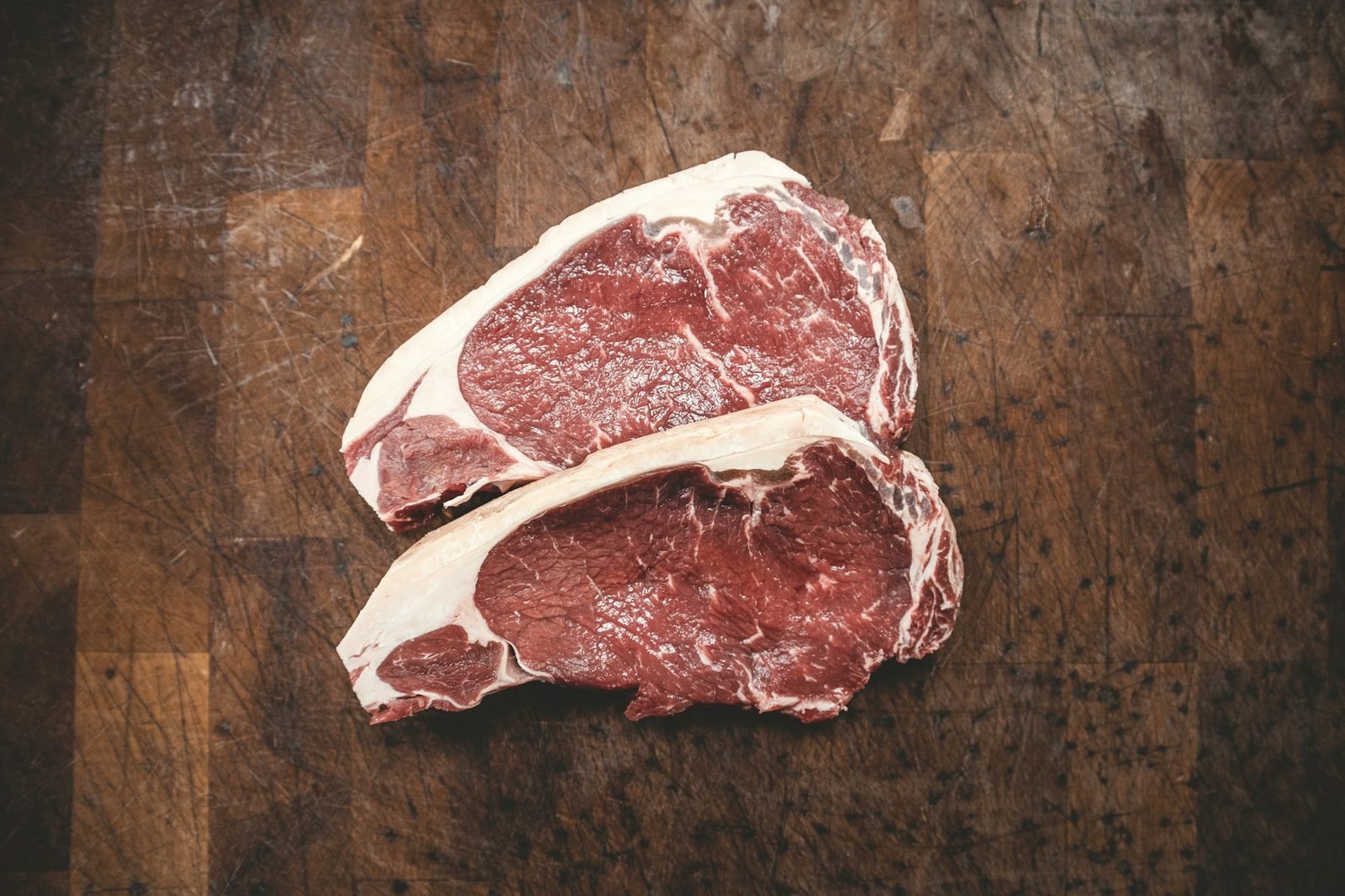 Two raw New York strip steaks on a worn wooden butcher block