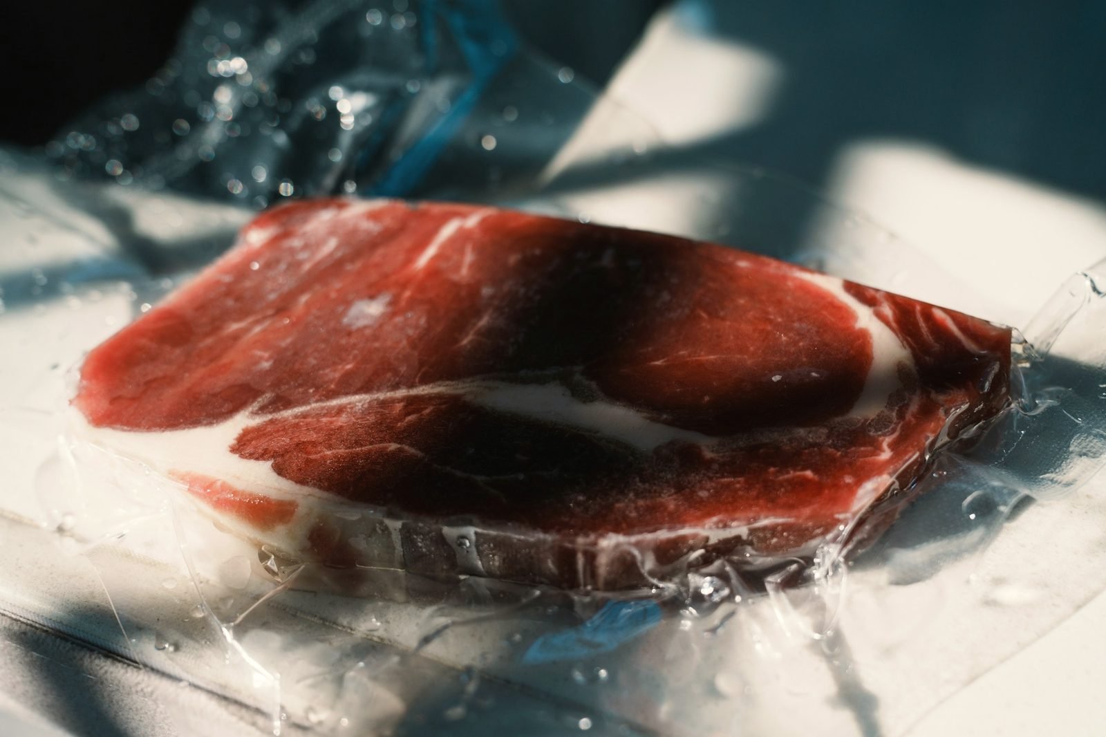 A marbled raw steak sealed in clear plastic in bright window light